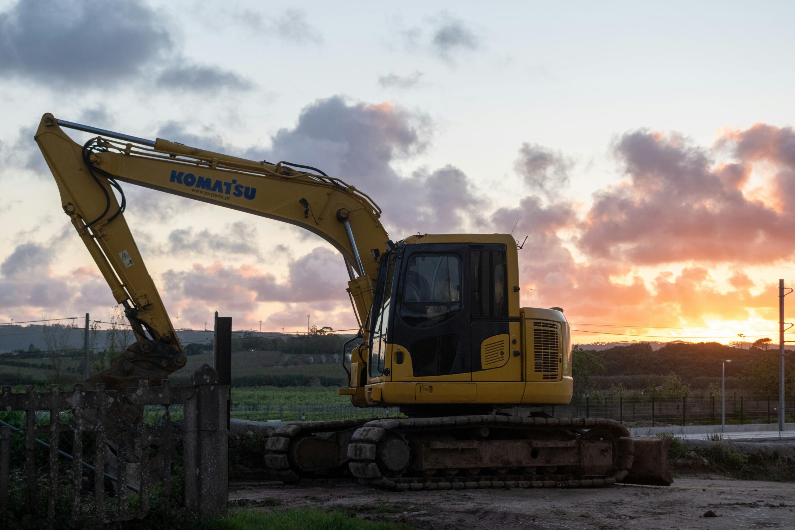 Silhouette of excavator working at sunset on a construction site with vibrant sky.
