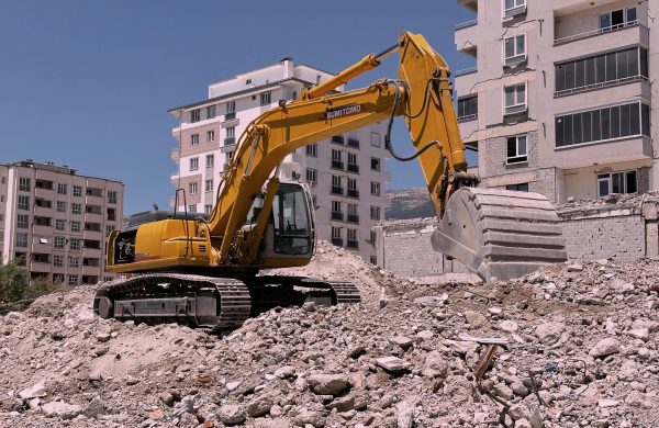 Yellow excavator working on urban construction site amidst rubble and buildings in Kahramanmaraş, Türkiye.